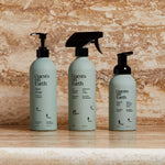 Three bottles of 'Guests on Earth' cleaning products on a wooden surface with a stone wall background.