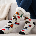 A person wearing cream knit socks with a colorful outdoor camping pattern, sitting on a light gray couch with a cream knit blanket.
