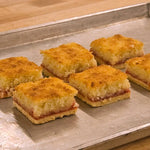 Six golden-brown baked bars with a crumbly topping and a red fruit filling, arranged on a metal baking sheet over a wooden surface.
